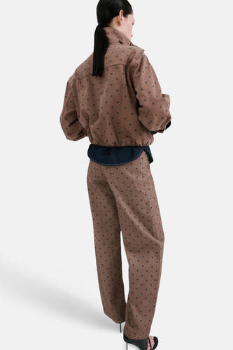 Bruine gekleurde jeans van MANGO, met een stippenpatroon, gecombineerd met een bijpassend jasje en zwarte hakken, vanuit een achteraanzicht.
