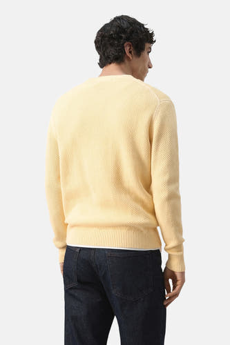 Gele trui met ronde hals van MANGO, achterkant, met een wafeltextuur en donkere jeans.
