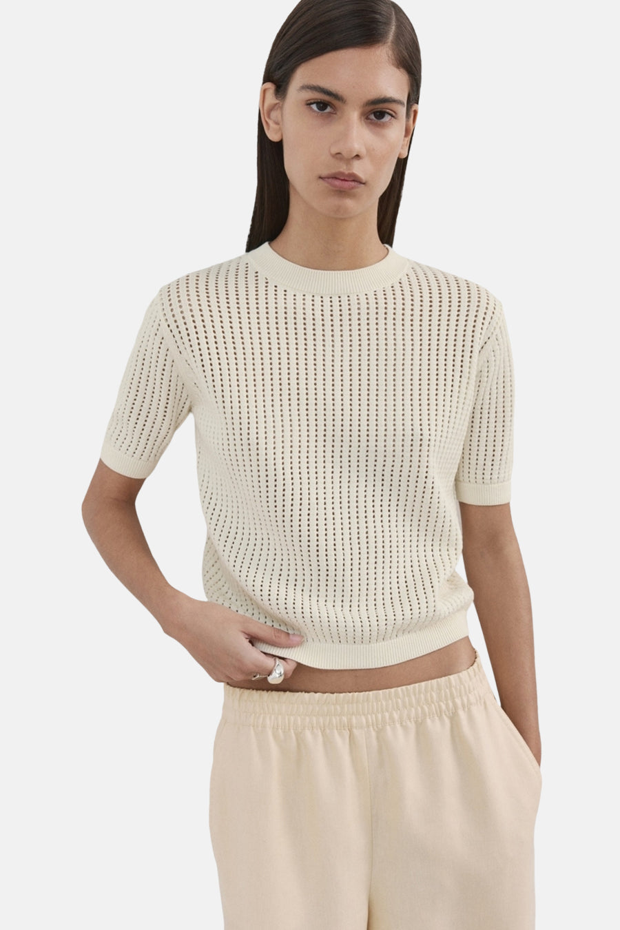 Pull beige à col rond de MANGO, à manches courtes et texture ajourée, porté avec un pantalon de couleur crème.