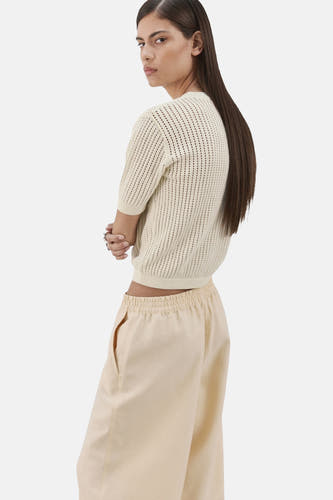 Beige trui met ronde hals van MANGO, met korte mouwen en opengebreide textuur, gedragen met crèmekleurige broek.
