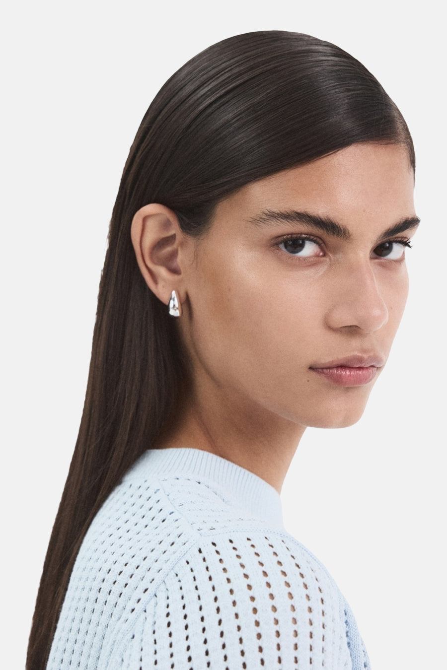 Pull bleu à col rond de MANGO, avec motif ajouré, porté avec des boucles d'oreilles argentées.