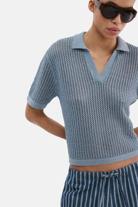Polo bleu à manches courtes de MANGO, avec une texture ajourée et porté avec un pantalon rayé.
