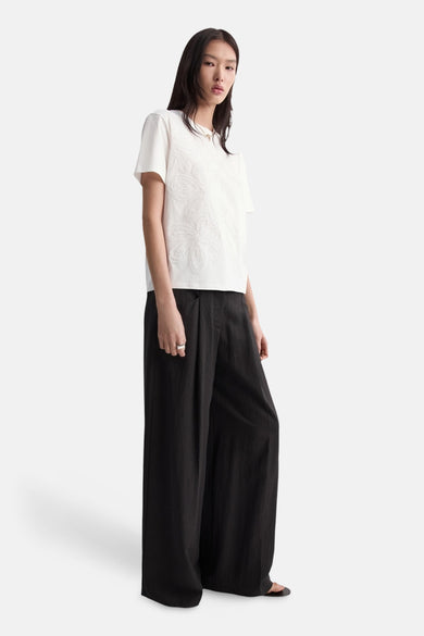 T-shirt blanc à manches courtes de MANGO, orné de subtils détails floraux sur le devant. Porté avec un pantalon noir ample.