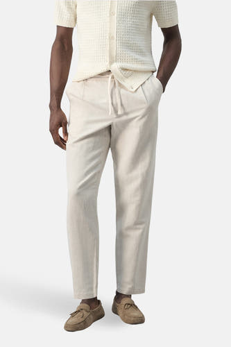 Pantalon écru de MANGO, combiné avec un polo en maille de couleur claire et des mocassins marron.