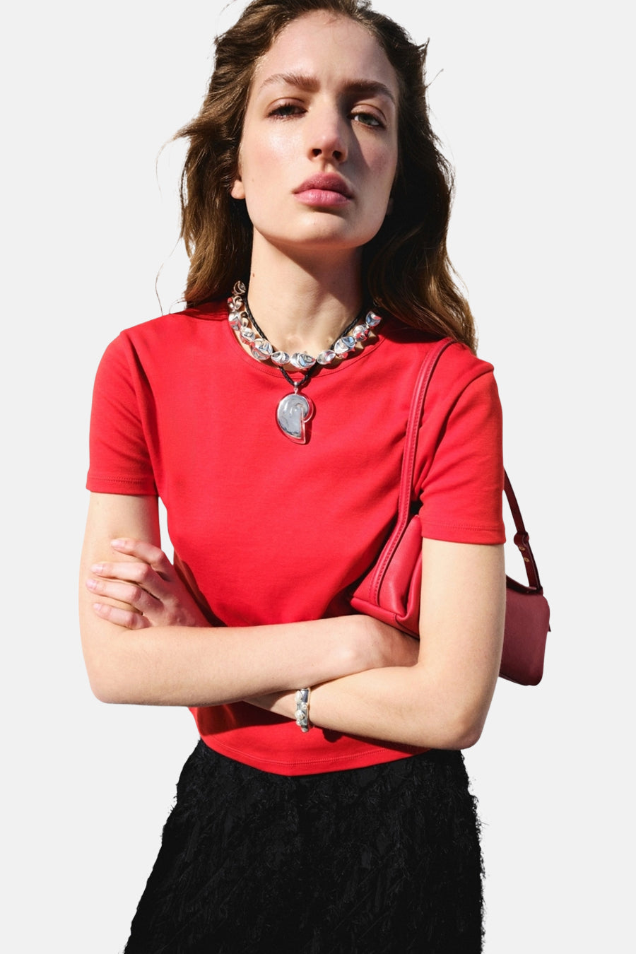 T-shirt rouge de MANGO, vu de dos sur un mannequin portant une jupe noire à franges et un bracelet argenté.