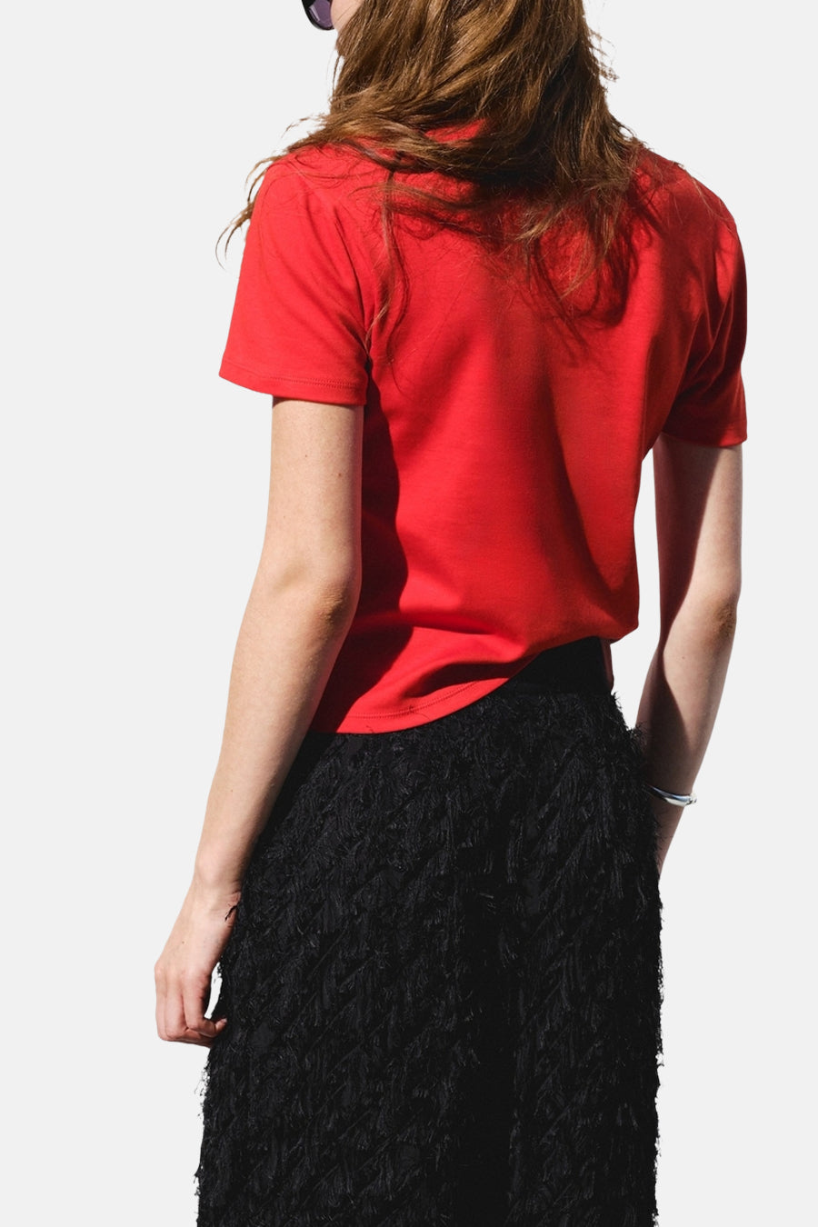 Rood T-shirt van MANGO, gezien van achteren op een model met een zwarte franjerok en zilveren armband.