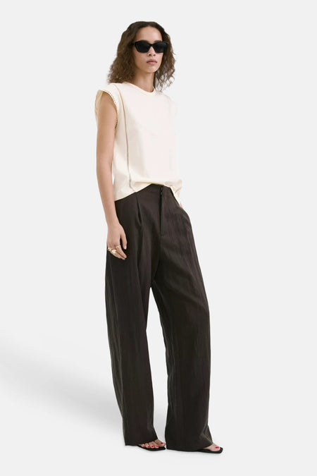 Beige mouwloze top van MANGO met geborduurde randen, gedragen met donkere wijde broek en zonnebril, zijprofiel.