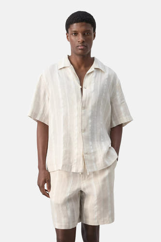 Chemise beige à manches courtes de MANGO, à rayures verticales, vue de dos, portée avec un short assorti.