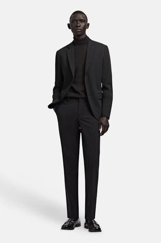 Pantalon de costume noir de MANGO, porté par un homme avec un blazer noir et un col roulé.