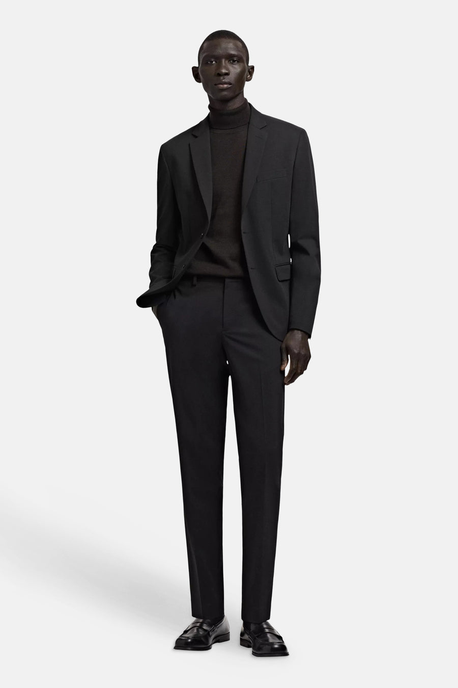 Pantalon de costume noir de MANGO, porté par un homme avec un blazer noir et un col roulé.