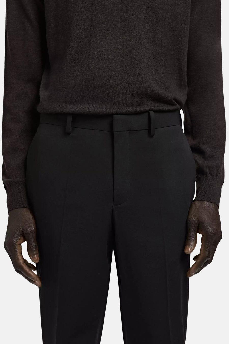 Pantalon de costume noir de MANGO avec passants de ceinture, porté avec un pull marron foncé.