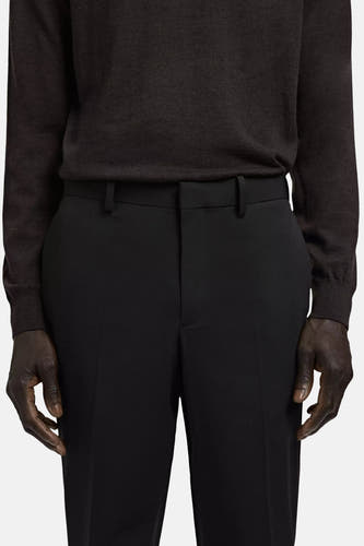 Pantalon de costume noir de MANGO avec un tissu lisse, porté avec un pull foncé et les mains visibles.