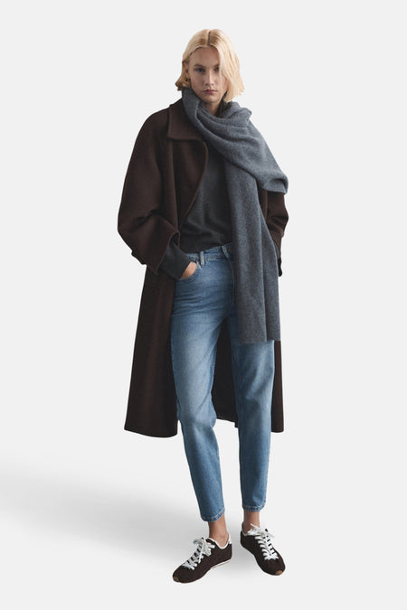 Jean mom bleu moyen de MANGO, associé à une longue veste brune, un pull gris et des baskets.