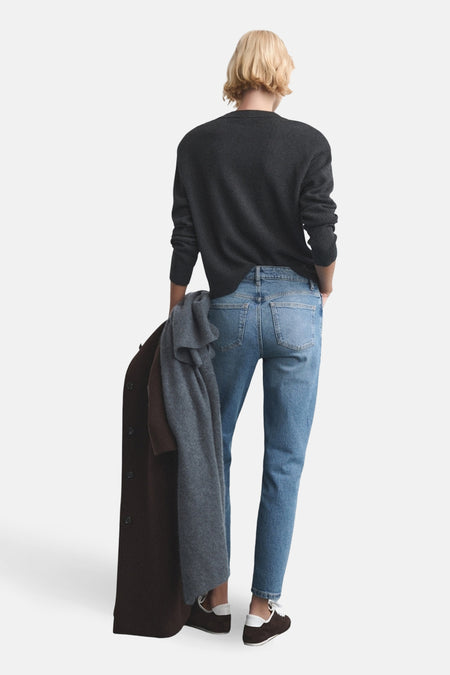 Mom jeans van blauw denim van MANGO, met achterzakken en gedragen met een grijze trui en donkerbruine schoenen.