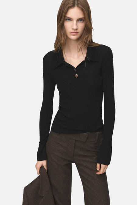 Vrouw met een zwarte geribbelde top met lange mouwen en bruine wollen broek.