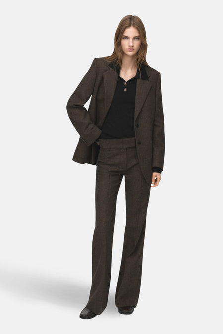 Vrouw in bruin tweedpak met zwarte polo en lakleren schoenen, staand.
