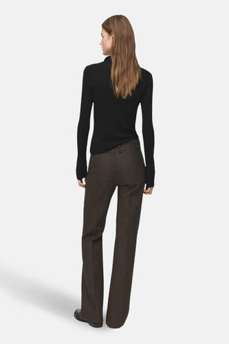 Zwarte trui met ronde hals van MANGO, op de rug gezien, gecombineerd met bruine wollen pantalon.
