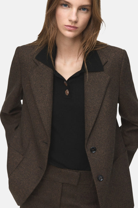 Vrouw in bruin wollen blazer en zwarte polo.