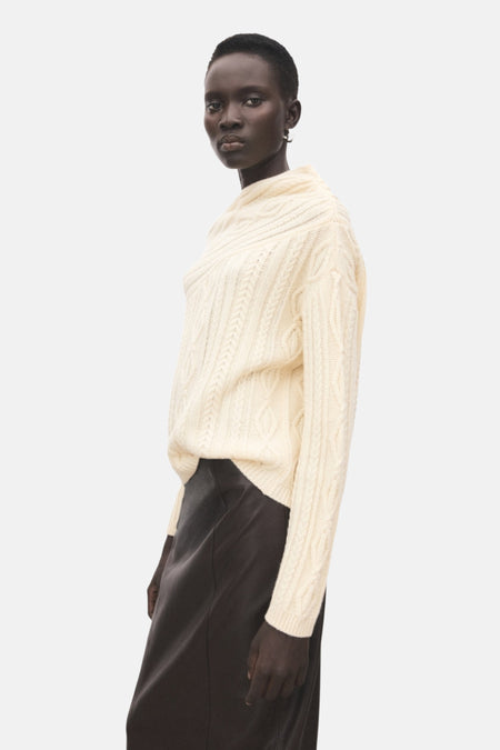 Model draagt crèmekleurige trui en bruine rok.
