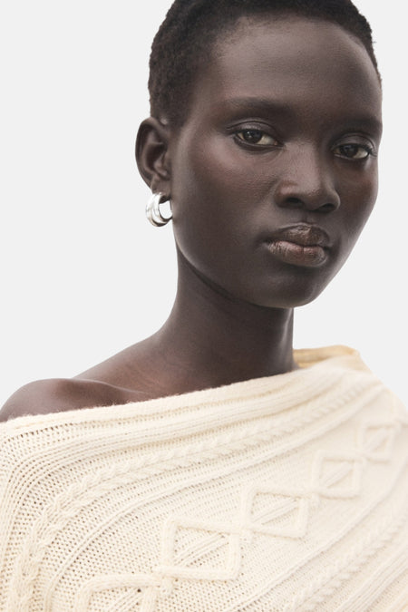 Portret van vrouw met crèmekleurige trui en zilveren oorringen.
