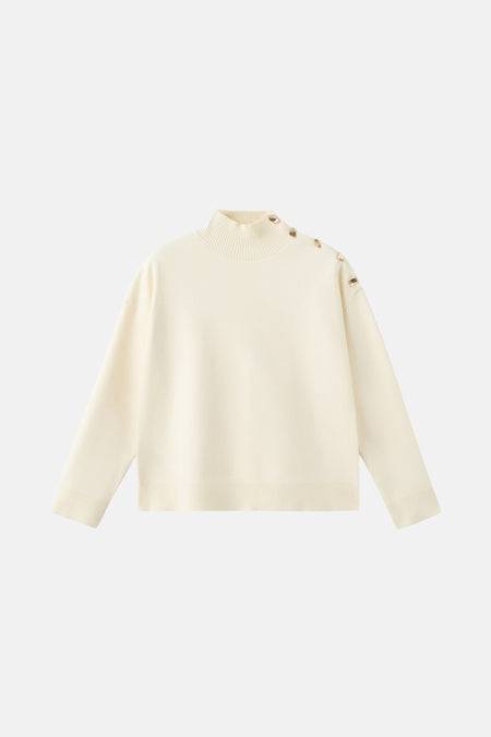 Gebroken witte trui met hoge kraag en gouden details op de schouder.
