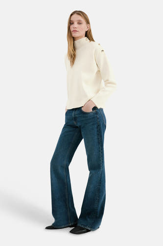 Pull col rond écru de MANGO, avec boutons dorés décoratifs sur les épaules, combiné avec un jean bleu à jambes larges.