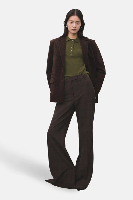 Vrouw in bruine blazer, olijfgroene polo en bruine uitlopende broek.