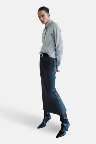 Sweat-shirt gris à col rond de MANGO, porté avec une longue jupe, une ceinture et des bottes noires à talon.