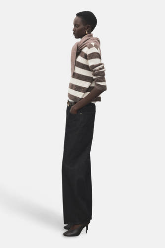 Sweat-shirt multicolore à col rond de MANGO, avec des rayures horizontales et associé à des jeans foncés et des baskets.