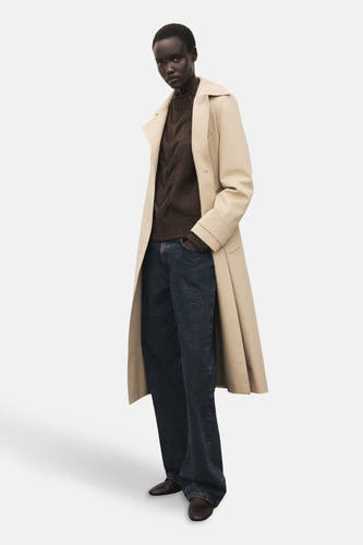 Pull marron avec col rond de MANGO, porté sous un manteau trench beige avec des jambes de jeans bleu marine larges.