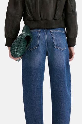 Jean en denim bleu moyen de MANGO, vu de dos, avec jambes larges et sac vert.