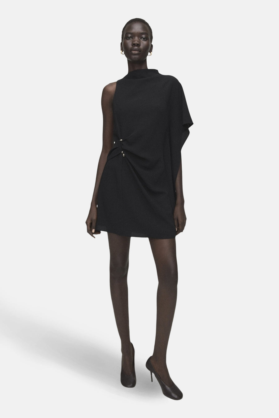 Robe noire sans manches de MANGO, avec une encolure asymétrique et un drapé décoratif sur le côté.