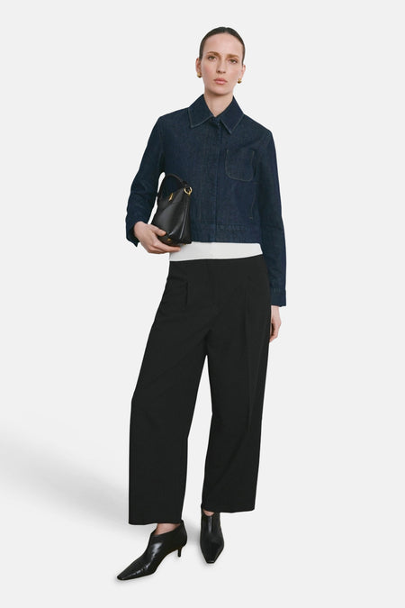 Pantalon noir de MANGO, à jambes larges et taille haute, combiné avec une veste en jean et des bottines en cuir noir.