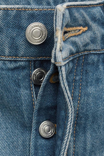 Jean en denim bleu moyen coupe spéciale de MANGO, gros plan sur la fermeture à boutons et les coutures.