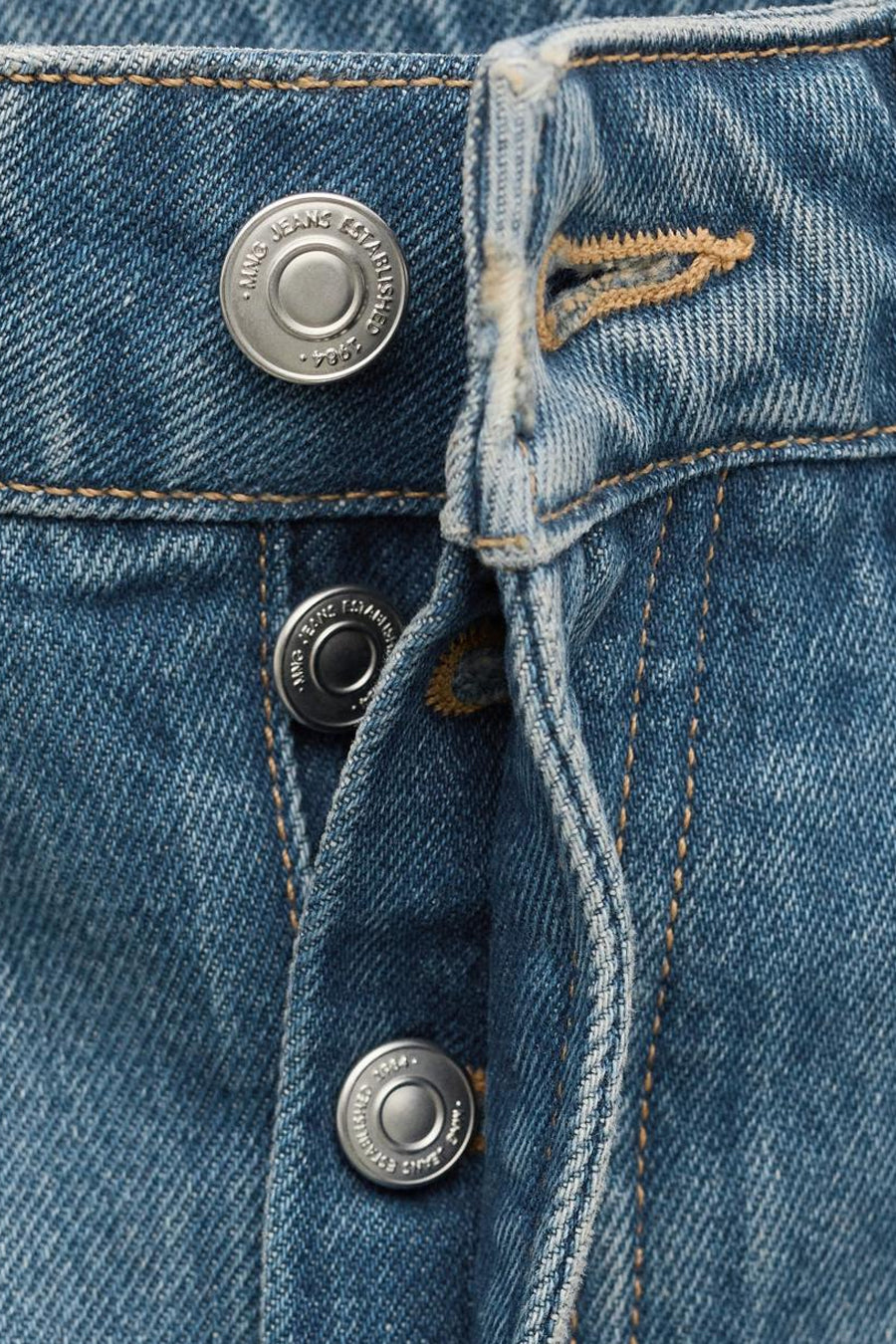 Jean en denim bleu moyen coupe spéciale de MANGO, gros plan sur la fermeture à boutons et les coutures.