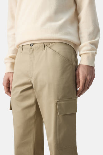 Pantalon beige de MANGO, avec poches cargo et fermeture à boutons, porté avec un pull de couleur crème.