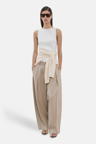Haut écru sans manches de MANGO, avec un gilet beige noué à la taille, combiné avec un pantalon large beige et des lunettes de soleil.