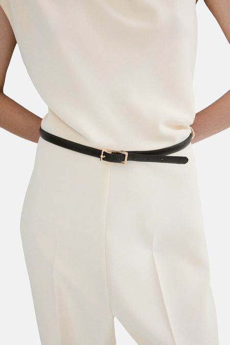 Ecru jumpsuit van MANGO, getailleerd met een dunne zwarte riem met gouden gesp en lange pijpen.
