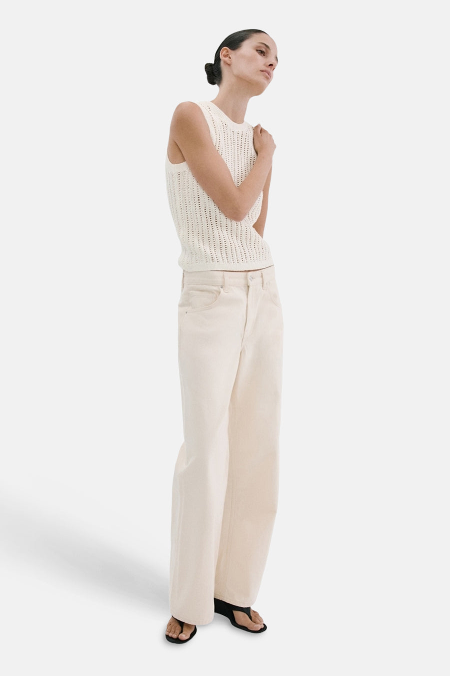 Haut sans manches écru de MANGO, avec une texture en maille ajourée, associée à un jean large de couleur crème et des sandales.