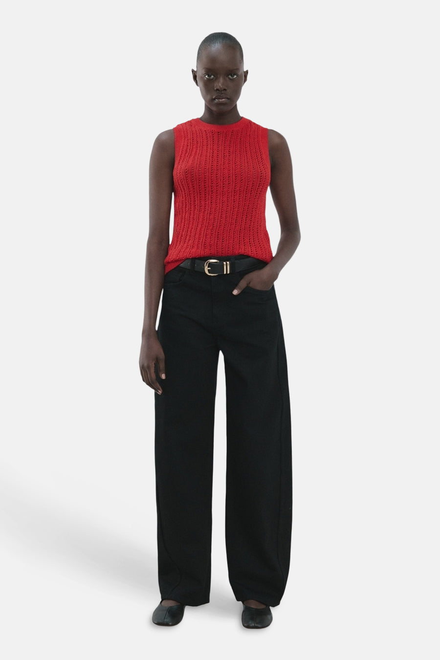 Haut rouge sans manches de MANGO, avec une texture en maille ajourée et combinée avec un pantalon noir et une ceinture.
