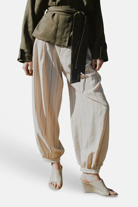 Pantalon écru de MANGO avec fines rayures verticales, coupe ample et chevilles élastiques.