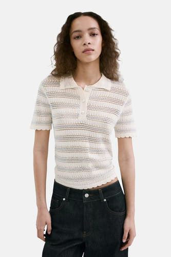 Polo écru de MANGO avec tissu tricoté rayé, manches courtes et bords festonnés, porté sur un mannequin avec un jean foncé.