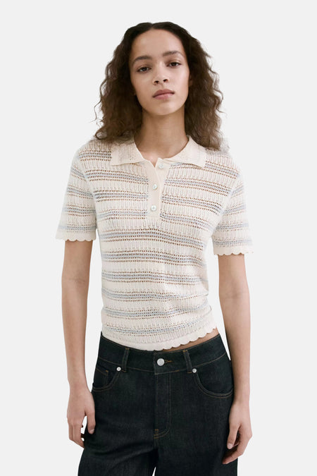 Polo écru de MANGO avec tissu tricoté rayé, manches courtes et bords festonnés, porté sur un mannequin avec un jean foncé.
