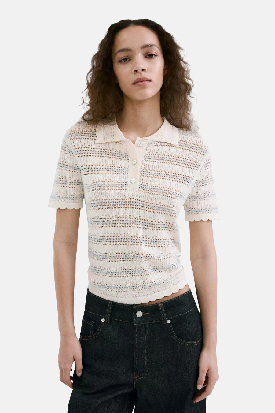 Polo écru de MANGO avec tissu tricoté rayé, manches courtes et bords festonnés, porté sur un mannequin avec un jean foncé.