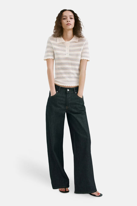 Polo en tricot écru de MANGO à rayures, col et bords festonnés, portée par un mannequin avec un jean foncé.