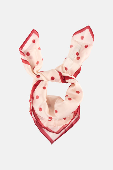 Écharpe d'été rose clair à pois rouges de MANGO, pliée et bordée d'une bordure rouge.