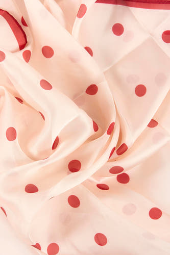 Écharpe d'été rose clair de MANGO avec des pois rouges, drapée de manière ondulée.