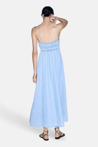 Lichtblauw denimkleedje zonder mouwen van MANGO, met smalle bandjes en geruchte taille, achterkant weergegeven, model draagt zwarte sandalen