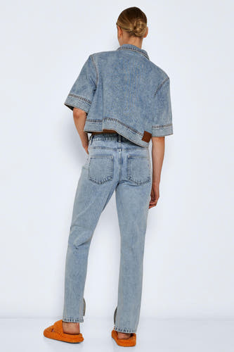 Jean droit en denim bleu clair de NOISY MAY, avec une fente sur le côté et porté avec un blouson en denim et des pantoufles orange.