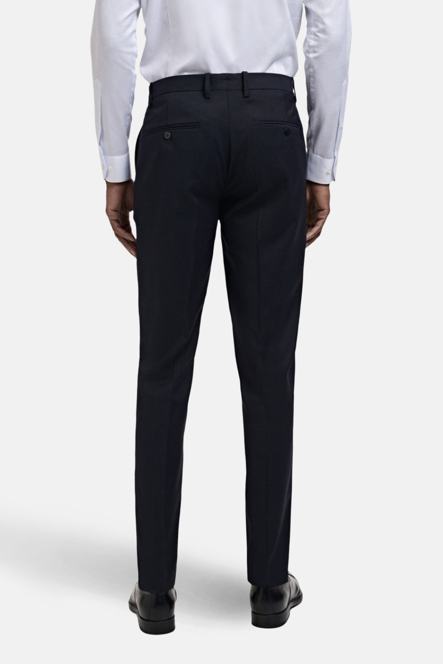 Achterkant van een man in een wit overhemd, donkerblauwe pantalon en zwarte leren schoenen.